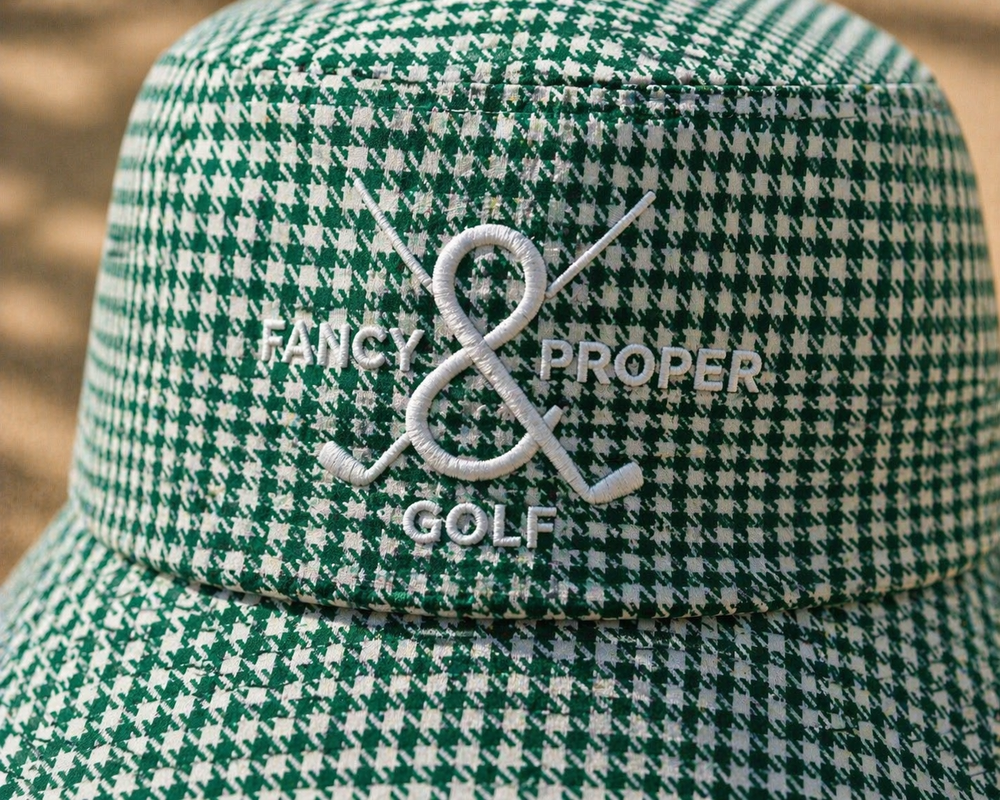 Green checkered bucket hat with branding on a sandy background