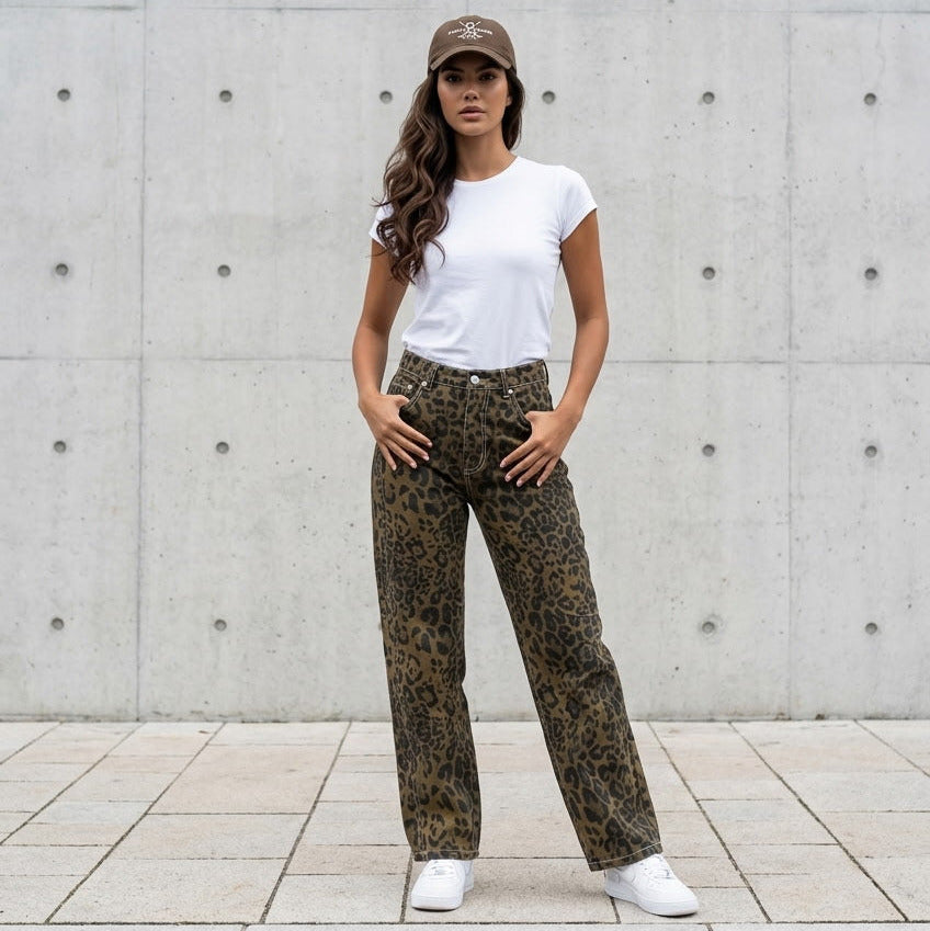 Woman wearing a white t-shirt, patterned pants, and a cap standing against a concrete wall.