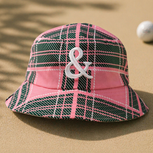 Pink and green plaid bucket hat with a white ampersand symbol on a beige background