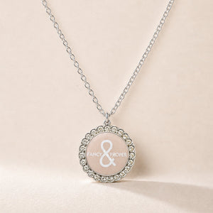 Necklace with a round pendant featuring a brand logo on a beige background