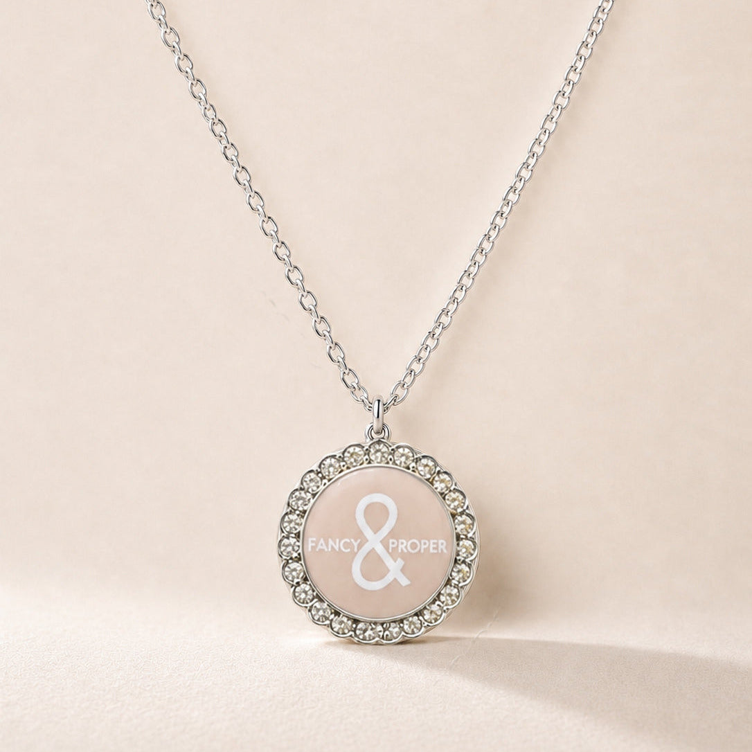 Necklace with a round pendant featuring a brand logo on a beige background