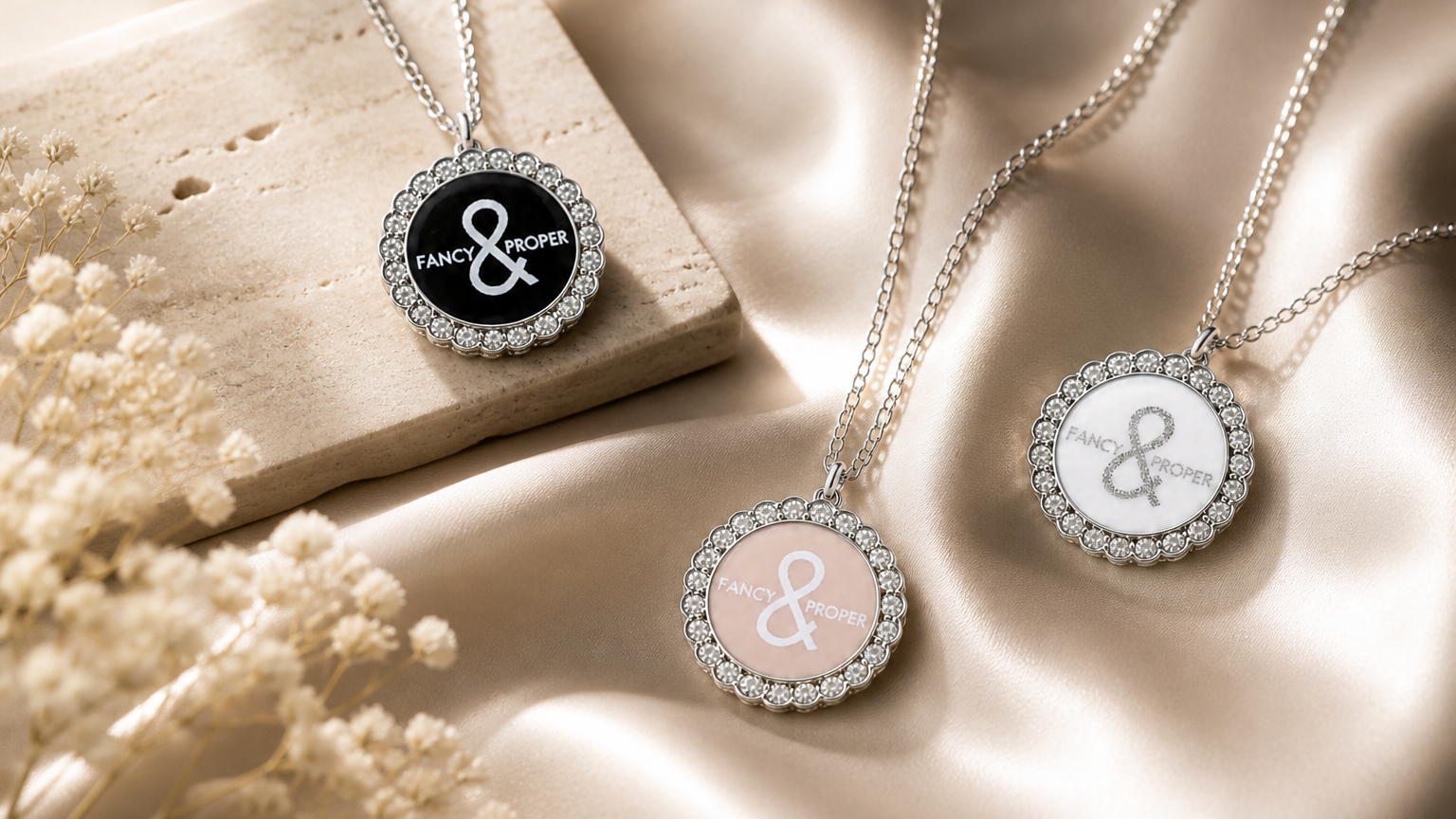 Three silver necklaces with circular pendants featuring ampersands on a beige surface.