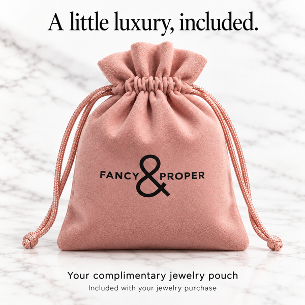 Upright blush pink Fancy & Proper complimentary jewelry pouch with black ampersand logo.