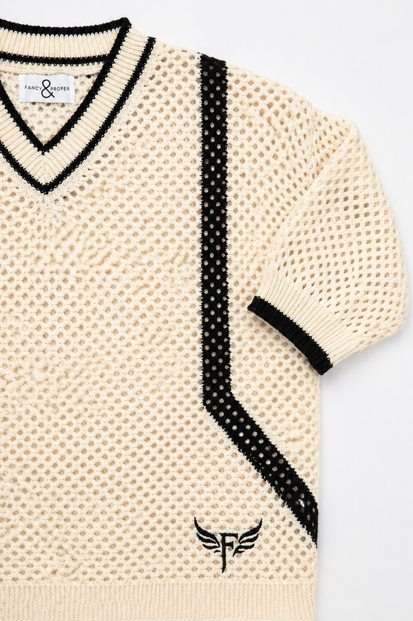 Beige sweater with black polka dot accents and a brand logo on a light gray background